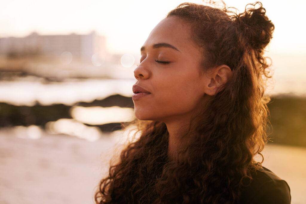 Shot of an attractive young woman alone on a beach meditating at sunset.