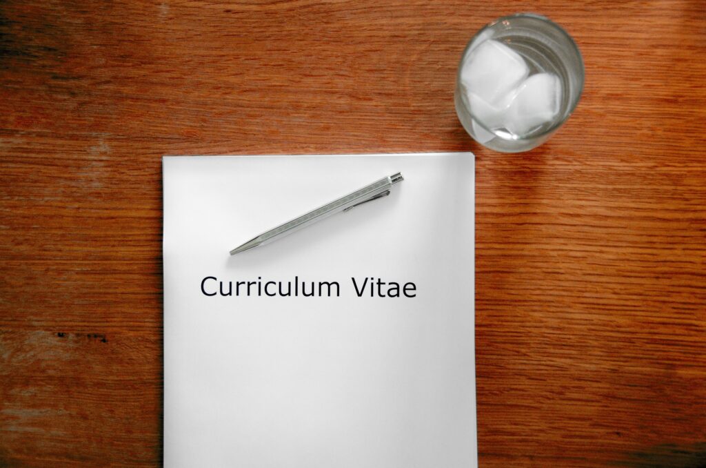 White A4 paper with the words Curriculum Vitae with a pen resting on top. A glass of water with ice nearby.