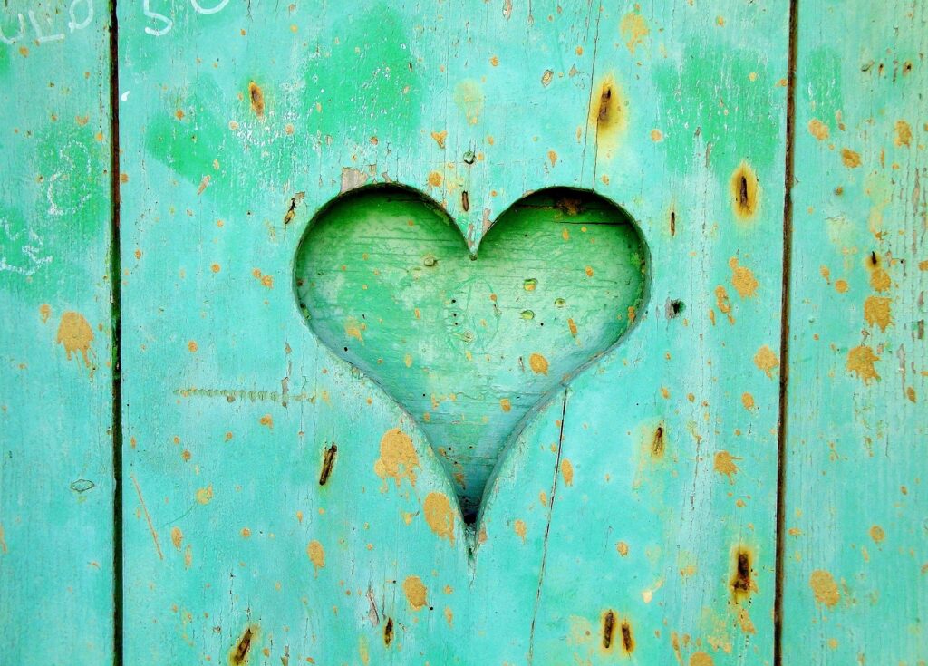 Heart shape carved out into a green wood panel which has rust marks and paint splatters.