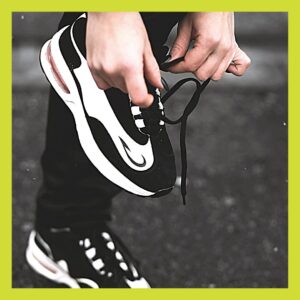 Close up of feet in black and white trainers, the person is tying up the laces on the right foot.