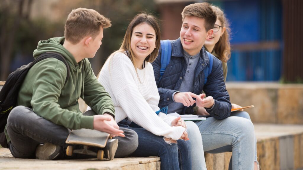 Group of 4 university students, sat outside smiling on a bench