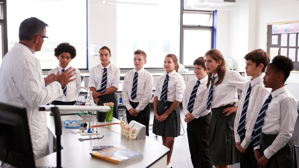 8 young students stood in row listening to teacher in science lab