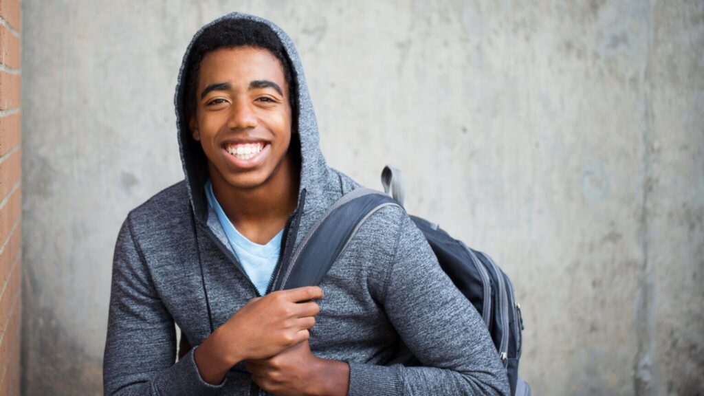 Teenage boy smiling broadly, with a hoodie and rucksack on