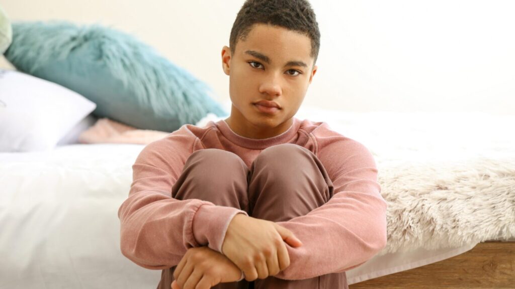 Sad teen boy sat on floor with his knees pulled into his chest and his arms wrapped around them. - gender blog