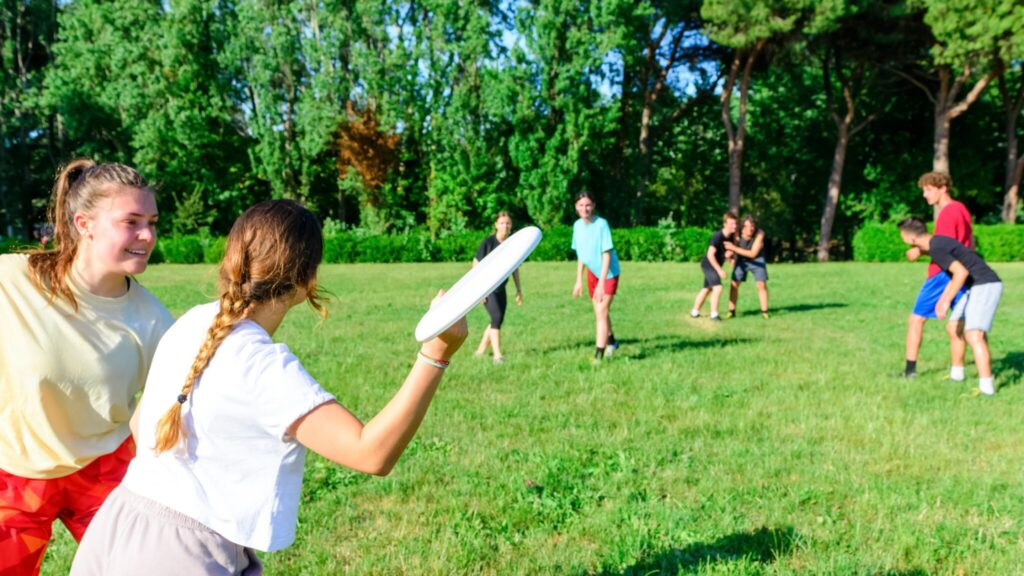 8 young people playing frisbee outdoors in a grassy field in summer