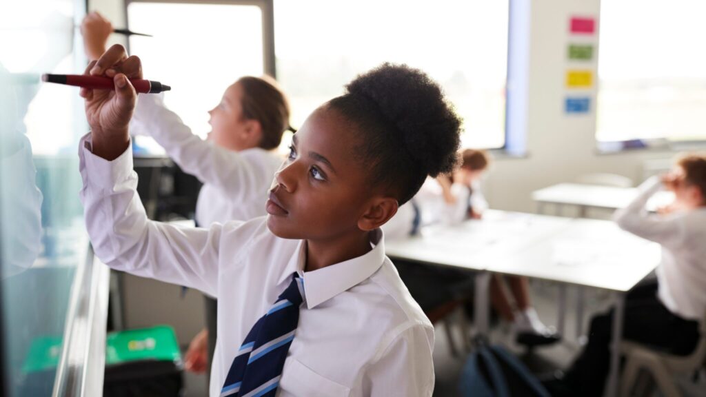 Two students at the front of a classroom using an interactive whiteboard
