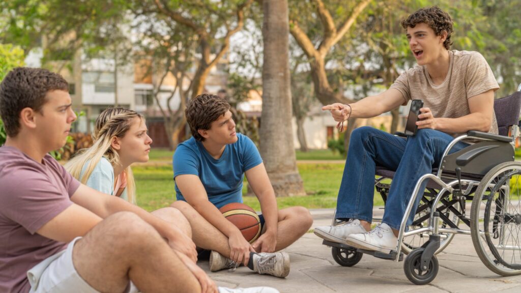 Group of 4 friends sat together talking. One of them is is sat in a wheelchair