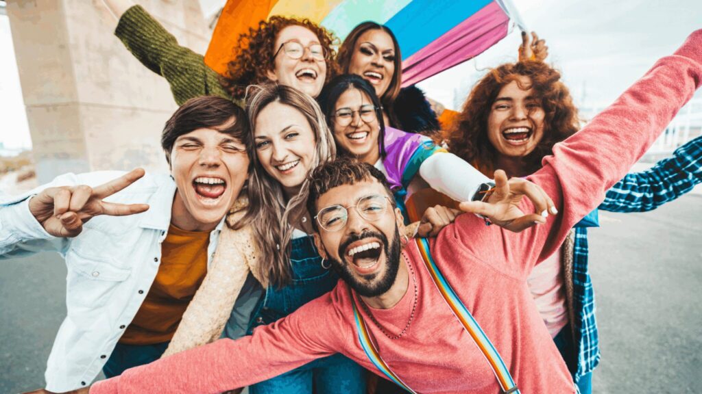 Group of teenagers and young adults smiling at the camera, showing off pride flags