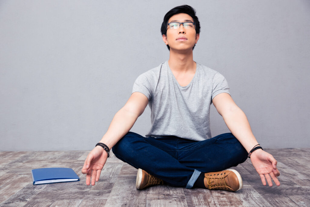 Young male with glasses sat cross legged in a meditating pose