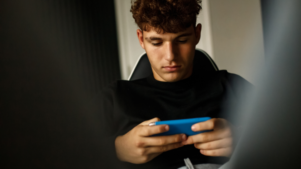 Teen boy looking down glumly at his mobile phone - social media blog