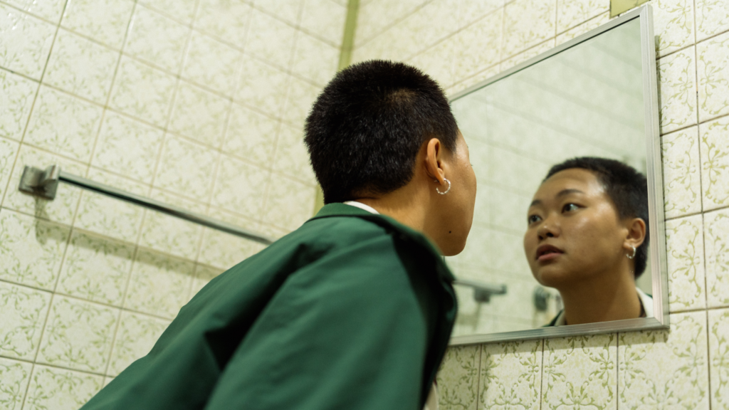 Non-binary teenage looks closely in mirror at appearance