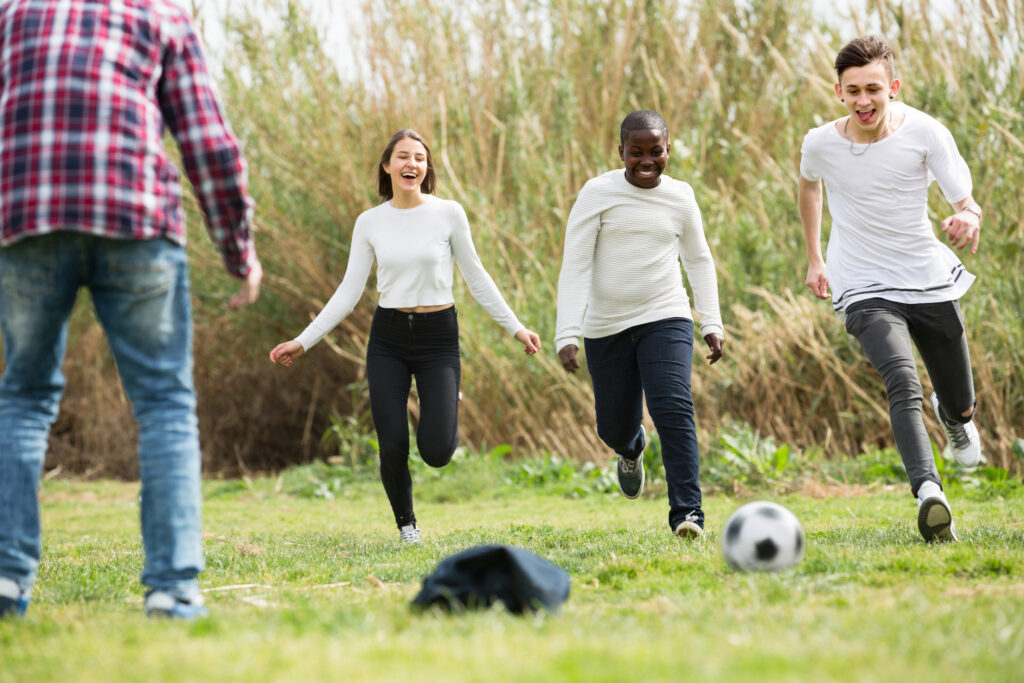Four young people playing football in a field with coats as goalposts