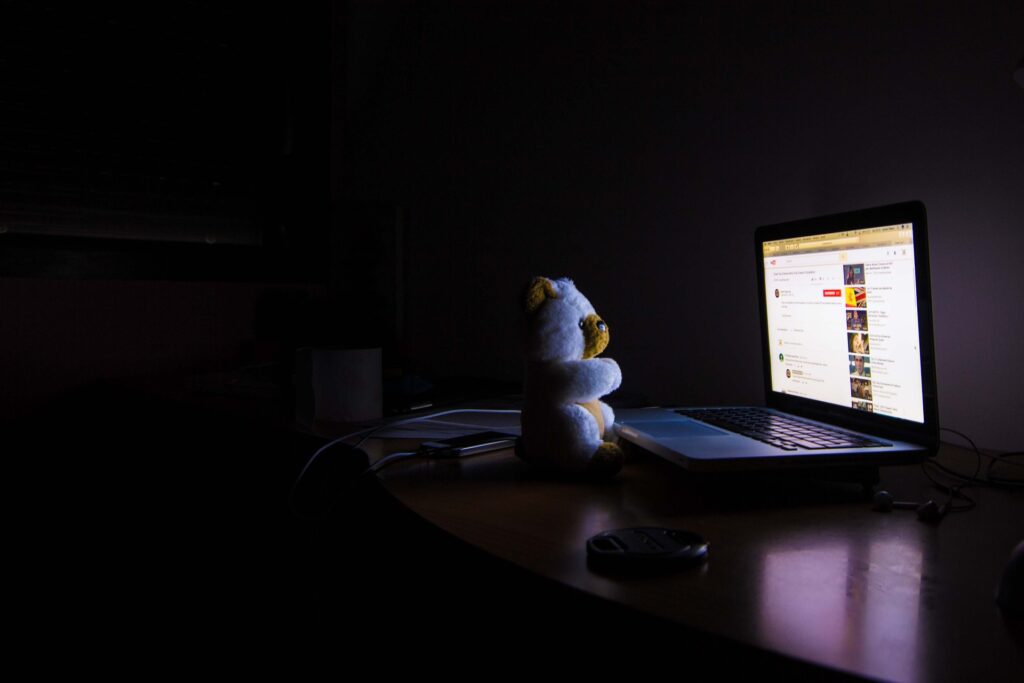 Teddy bear placed in front of a laptop in a dark room lit up by the screen