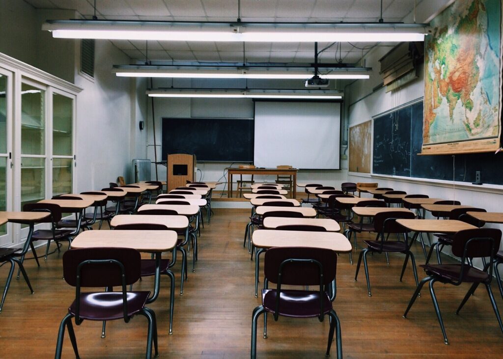 view from back of an empty classroom, individual chairs and desks in a row set out under exam conditions.