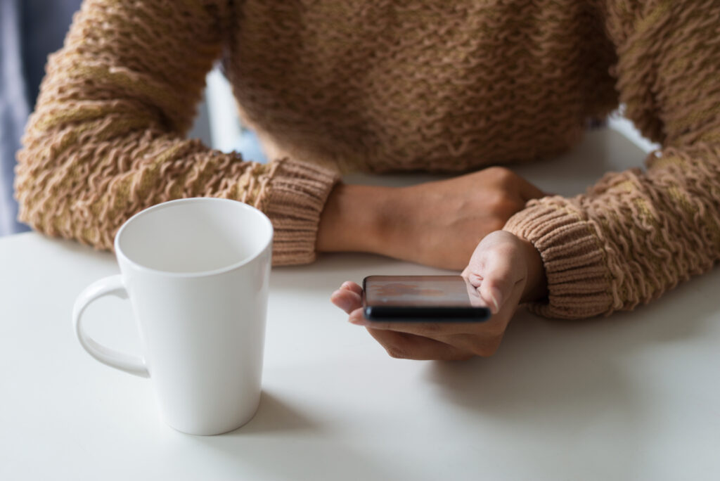 woman in a knit jumper on her phone with a warm drink