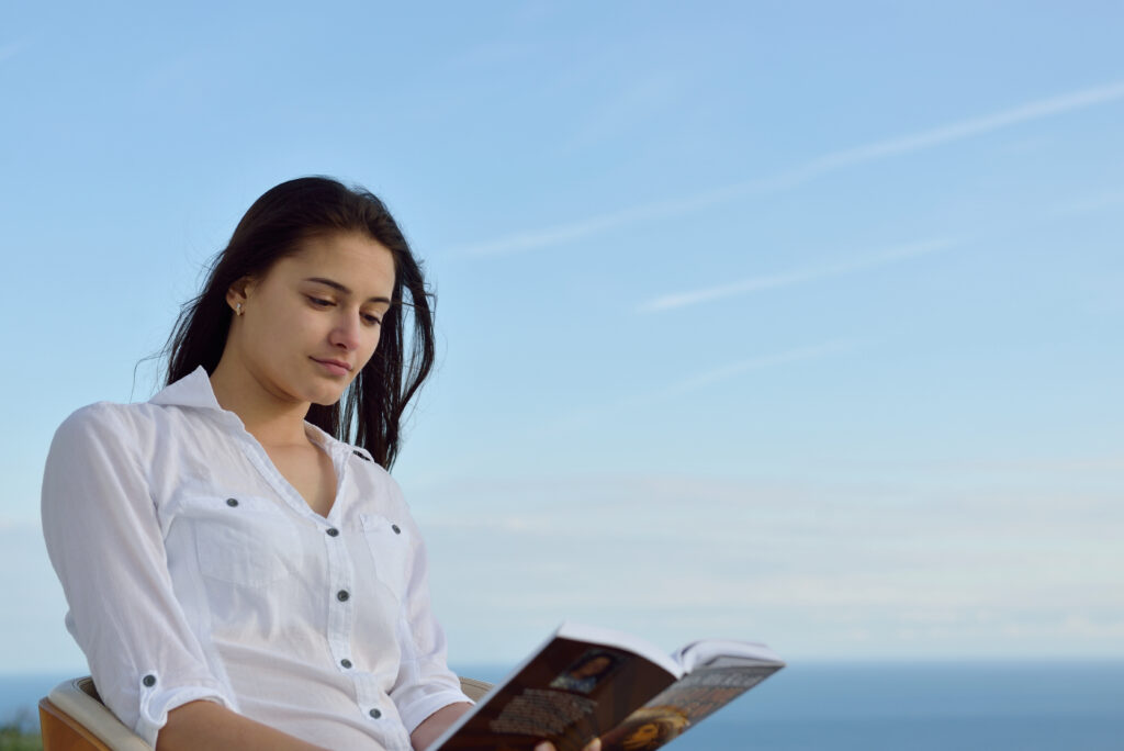 Young girl with the blue sky behind her reading a book