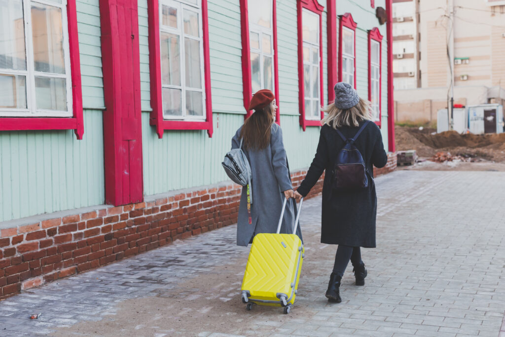 Two female friends walking with backpacks and a suitcase.