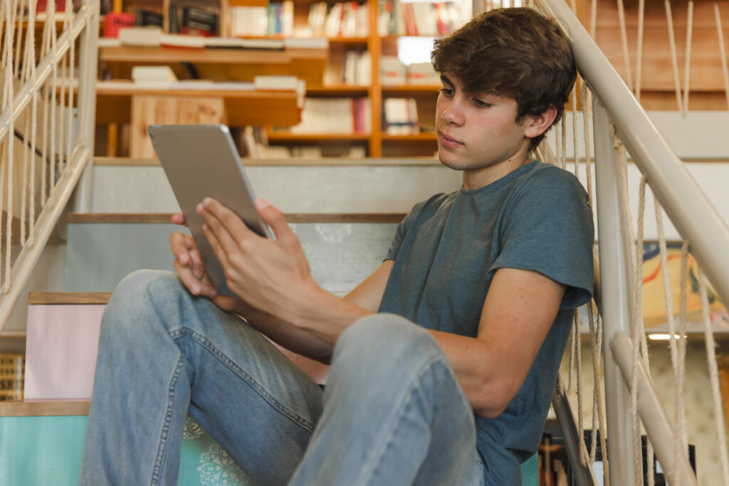 Teenage boy sitting on steps looking at his ipad. 