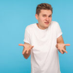 What do you want. Portrait of confused man in t-shirt expressing misunderstanding, gesturing in puzzlement with indignant face, asking why'd you do that. indoor studio shot isolated on blue background
