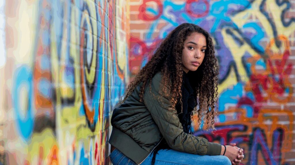 Black teenager in front of graffiti wall staring sadly