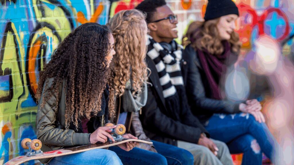 Group of teenagers sitting in front of the graffiti wall, talking with friends