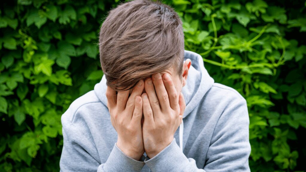 Teen boy sat slouched with his head in his hands