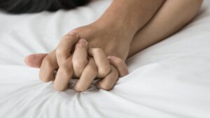 Two people with fingers interlocked on a bed