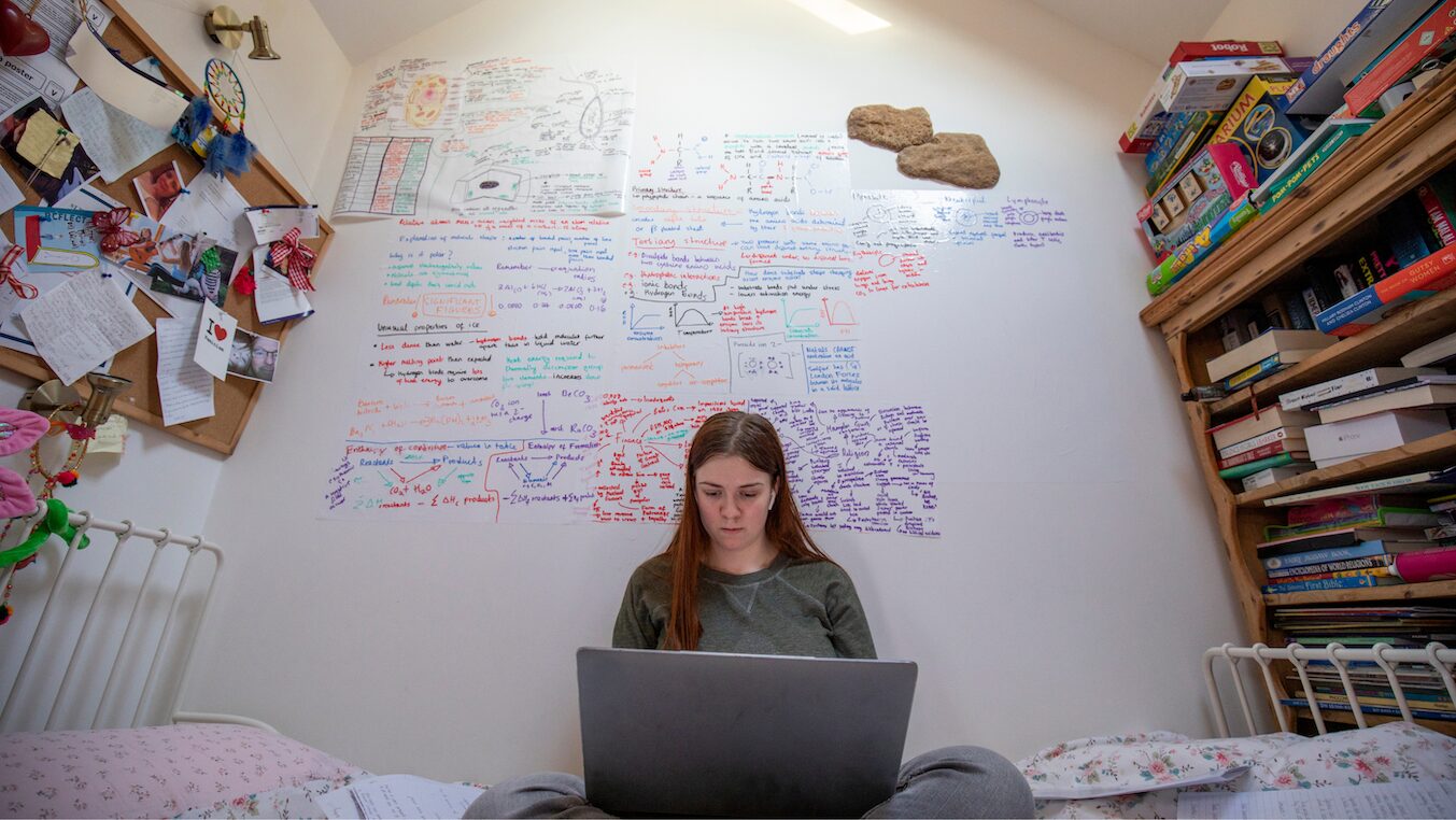 Teen girl revising alone in bedroom surrounding by revision notes