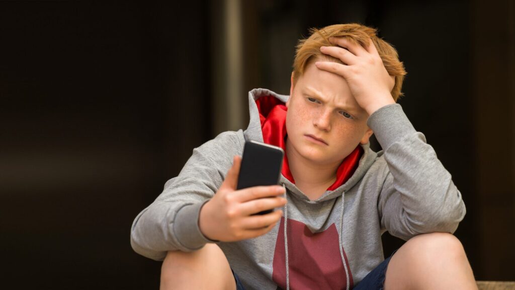 Boy sat on step looking upset at his phone