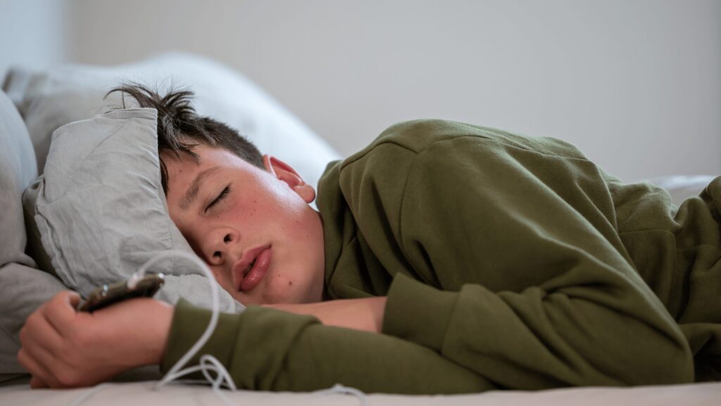 Teen boy sleeping in bed clutching onto his phone